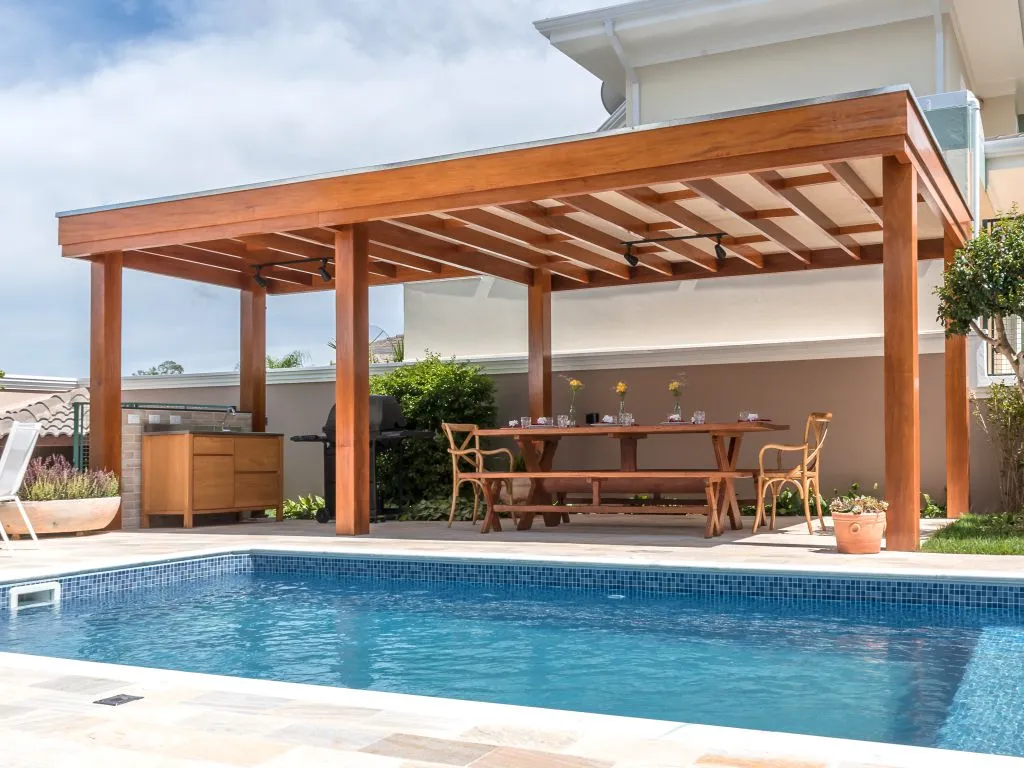 Pergolado de madeira anexado à casa, cobrindo área gourmet externa com piscina