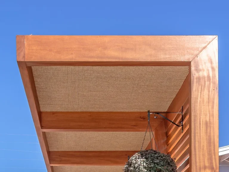 Pergolado em madeira com forro Solare Cobrire aplicado em área externa com jardim vertical.